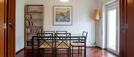 A dining area with a table and chairs, a bookshelf, a painting, and a floor lamp.