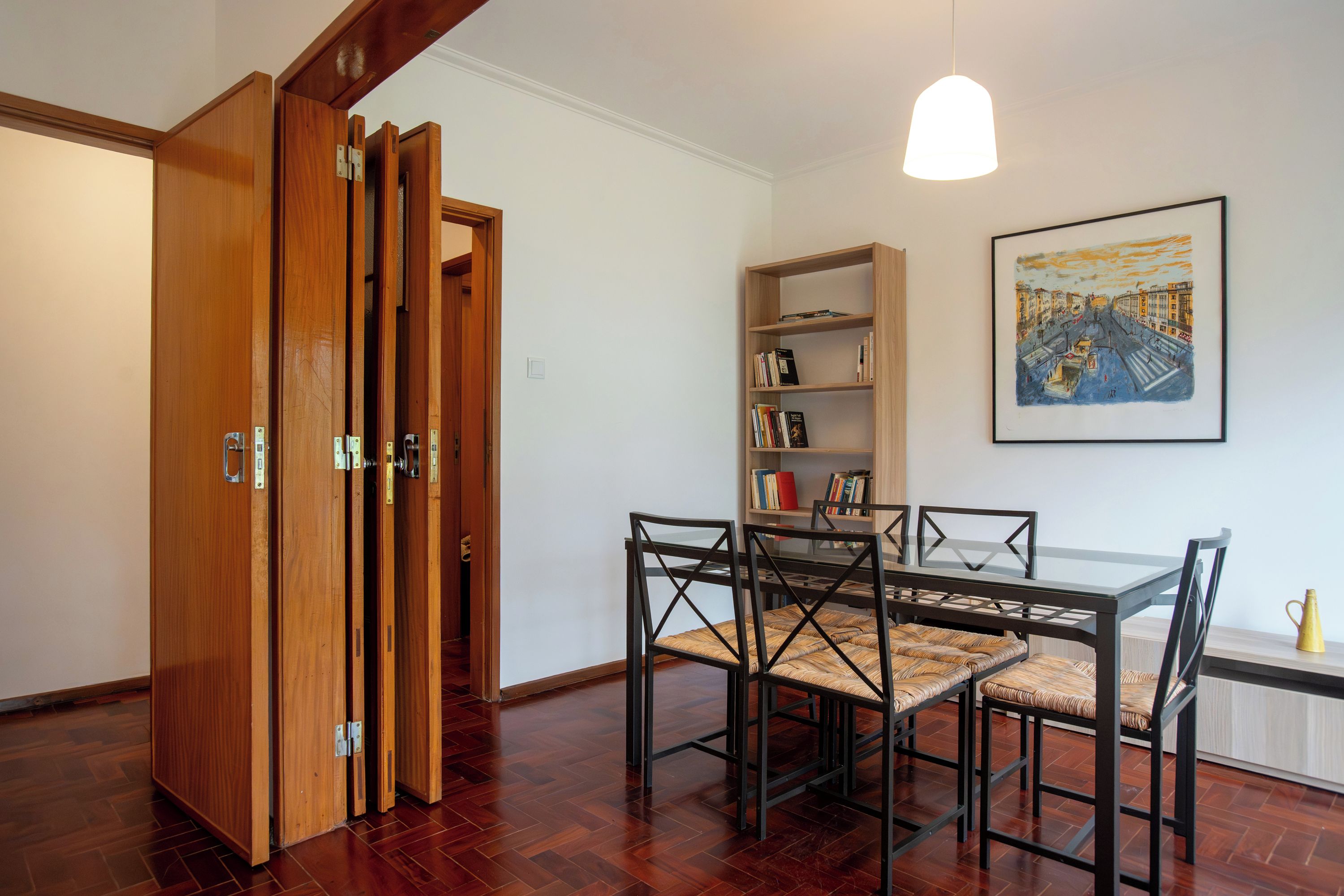 Un comedor con una mesa y sillas, una estantería y un cuadro en la pared.