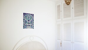 A bedroom with a white bed, a decorative wall hanging, and white louvered closets. - Magnificent seaside residence with a 50 m² rooftop terrace and 2 large balconies (Villanova)