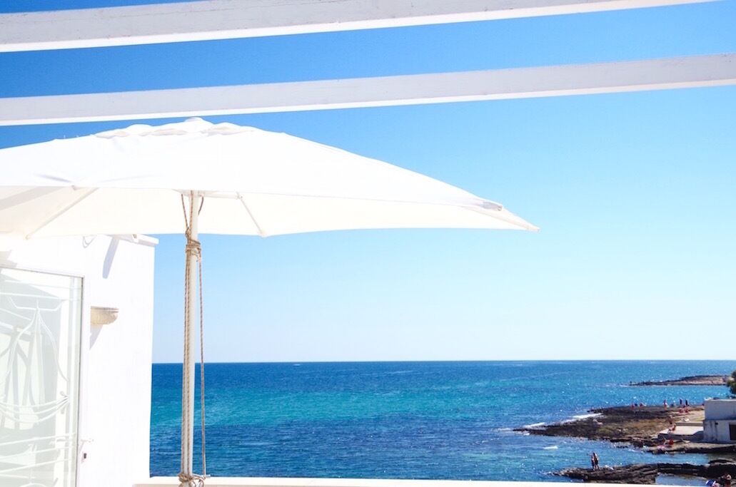 A balcony with a white umbrella overlooking a coastal view.