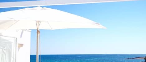 A balcony with a white umbrella overlooking a coastal view.