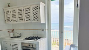 A kitchen with white cabinets, a gas stove, an oven, and a view of the ocean through a glass door. - Magnificent seaside residence with a 50 m² rooftop terrace and 2 large balconies (Villanova)