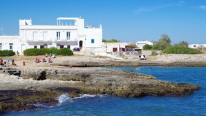 A coastal building with multiple balconies, a rocky shoreline, and people swimming in the water. - Magnificent seaside residence with a 50 m² rooftop terrace and 2 large balconies (Villanova)