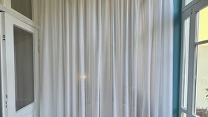 Ein Zimmer mit einem großen weißen Vorhang, Holzboden und einem Fenster mit Blick.