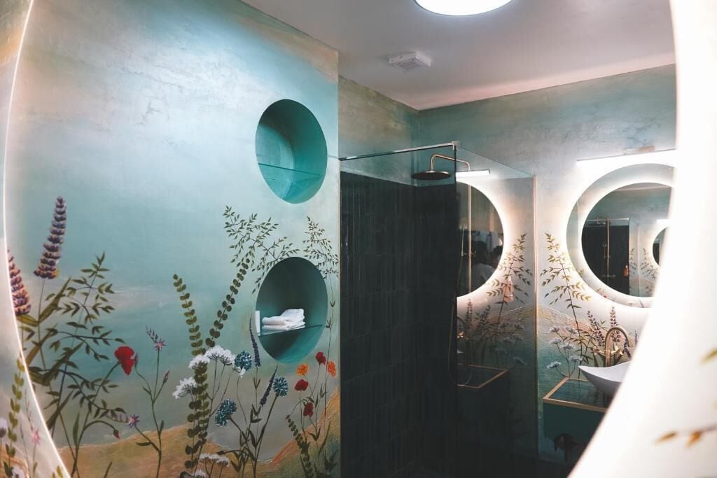 A bathroom with a mural of plants and flowers, a round mirror, and a shower area.