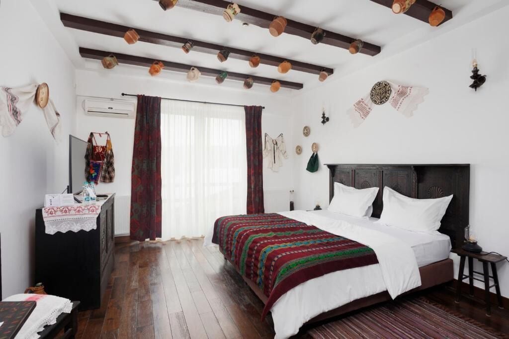 Ein Schlafzimmer mit Holzboden, einem Bett mit weißer Bettwäsche, einem Holzschrank und einem Fenster mit Vorhängen.