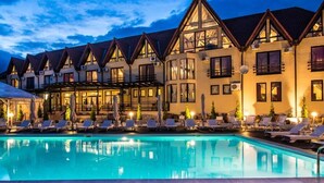 A hotel with a swimming pool, multiple balconies, and a well-lit exterior at dusk.