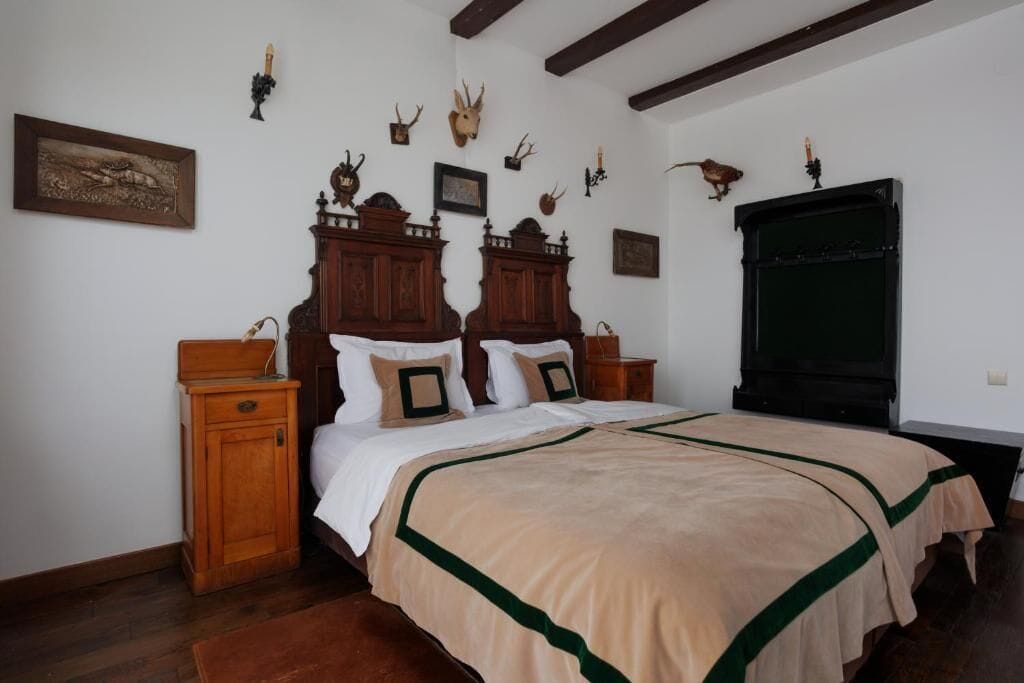 Une chambre à coucher avec un grand lit, une tête de lit en bois, deux tables de chevet et des décorations murales, notamment des têtes d’animaux.