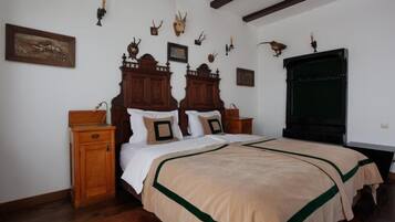 Une chambre à coucher avec un grand lit, une tête de lit en bois, deux tables de chevet et des décorations murales, notamment des têtes d’animaux.