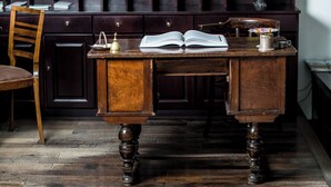 A wooden desk with an open book, a brass bell, and a small container with pencils.