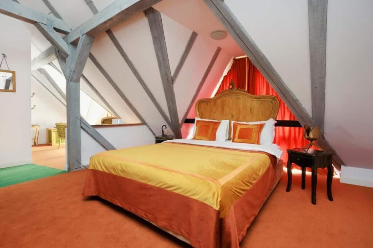 A bedroom with a sloped ceiling, a bed with a wooden headboard, and a nightstand with a lamp.