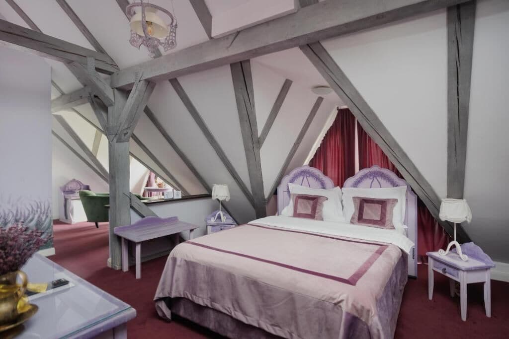 A bedroom with a large bed, a nightstand, a small table, and a window with curtains.