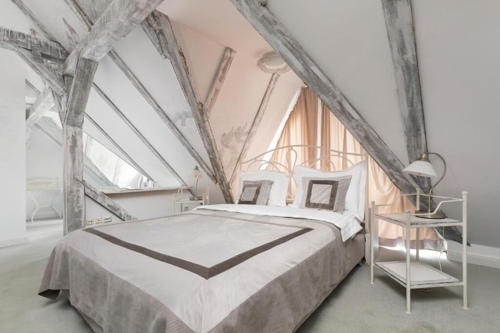 Une chambre à coucher avec un grand lit, une table de chevet, une lampe et une fenêtre avec des rideaux.