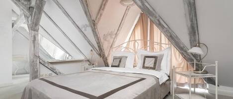 Une chambre à coucher avec un grand lit, une table de chevet, une lampe et une fenêtre avec des rideaux.