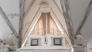 A bedroom with a high ceiling, a bed with white bedding, and curtains.