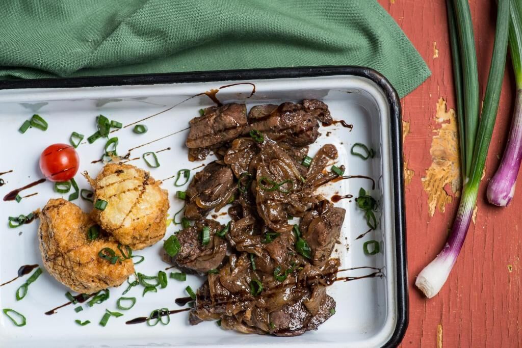A tray with grilled meat, a grilled vegetable, and a cherry tomato on a white plate.