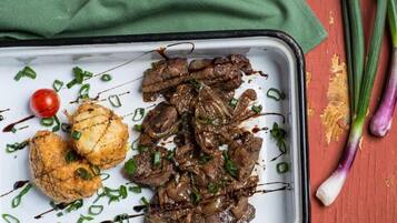 A tray with grilled meat, a grilled vegetable, and a cherry tomato on a white plate.