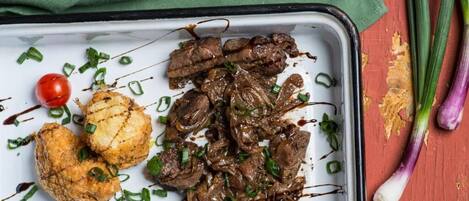 Ein Tablett mit gegrilltem Fleisch, gegrilltem Gemüse und einer Kirschtomate auf einem weißen Teller.