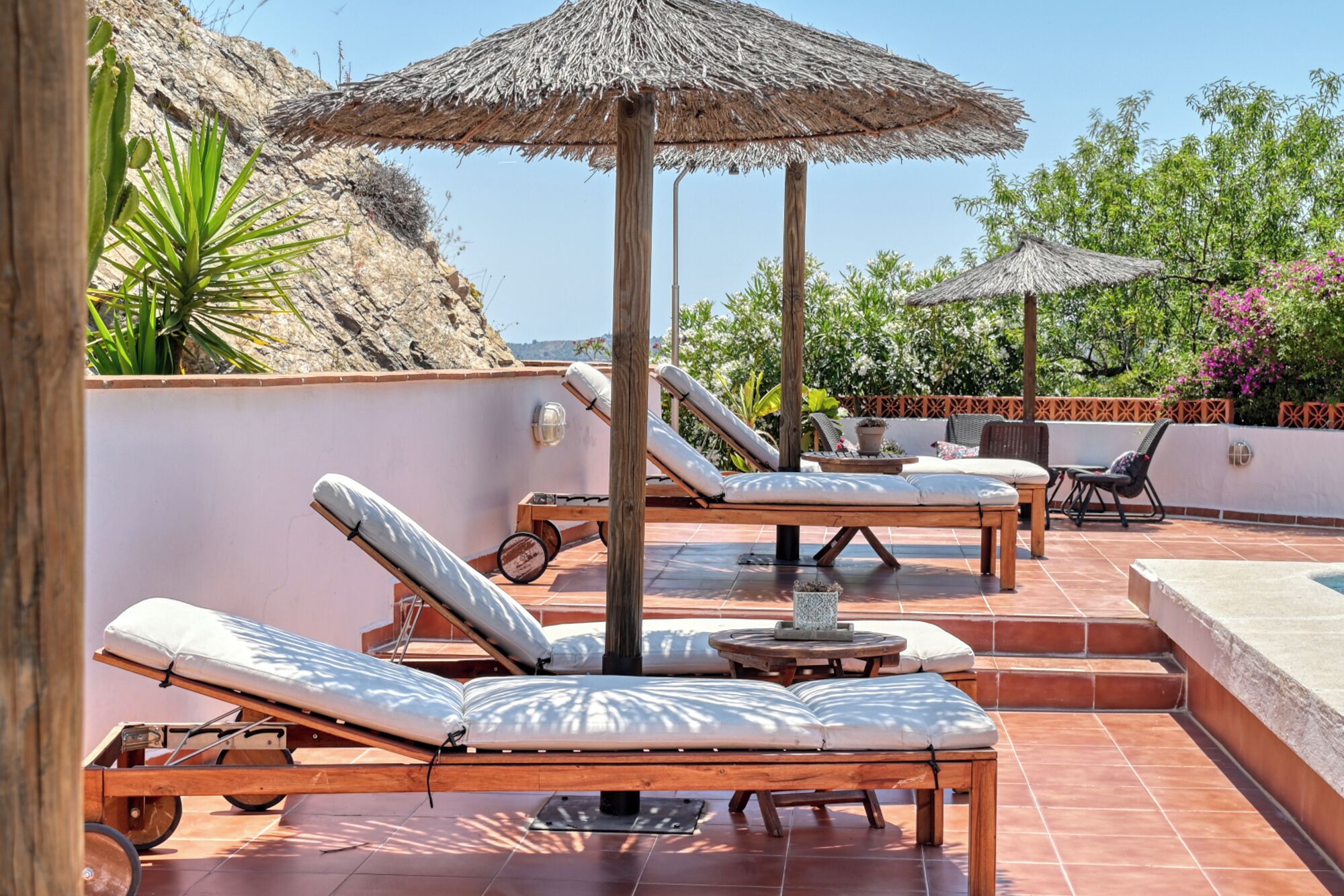 A rooftop terrace with sun loungers, a small table, and a thatched umbrella.