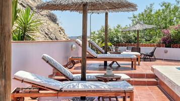 A rooftop terrace with sun loungers, a small table, and a thatched umbrella.