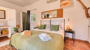 A bedroom with a bed, a nightstand, a mirror, a window with curtains, and a wall-mounted air conditioner. - Casa Azafranes Boutique B&B (Arenas)