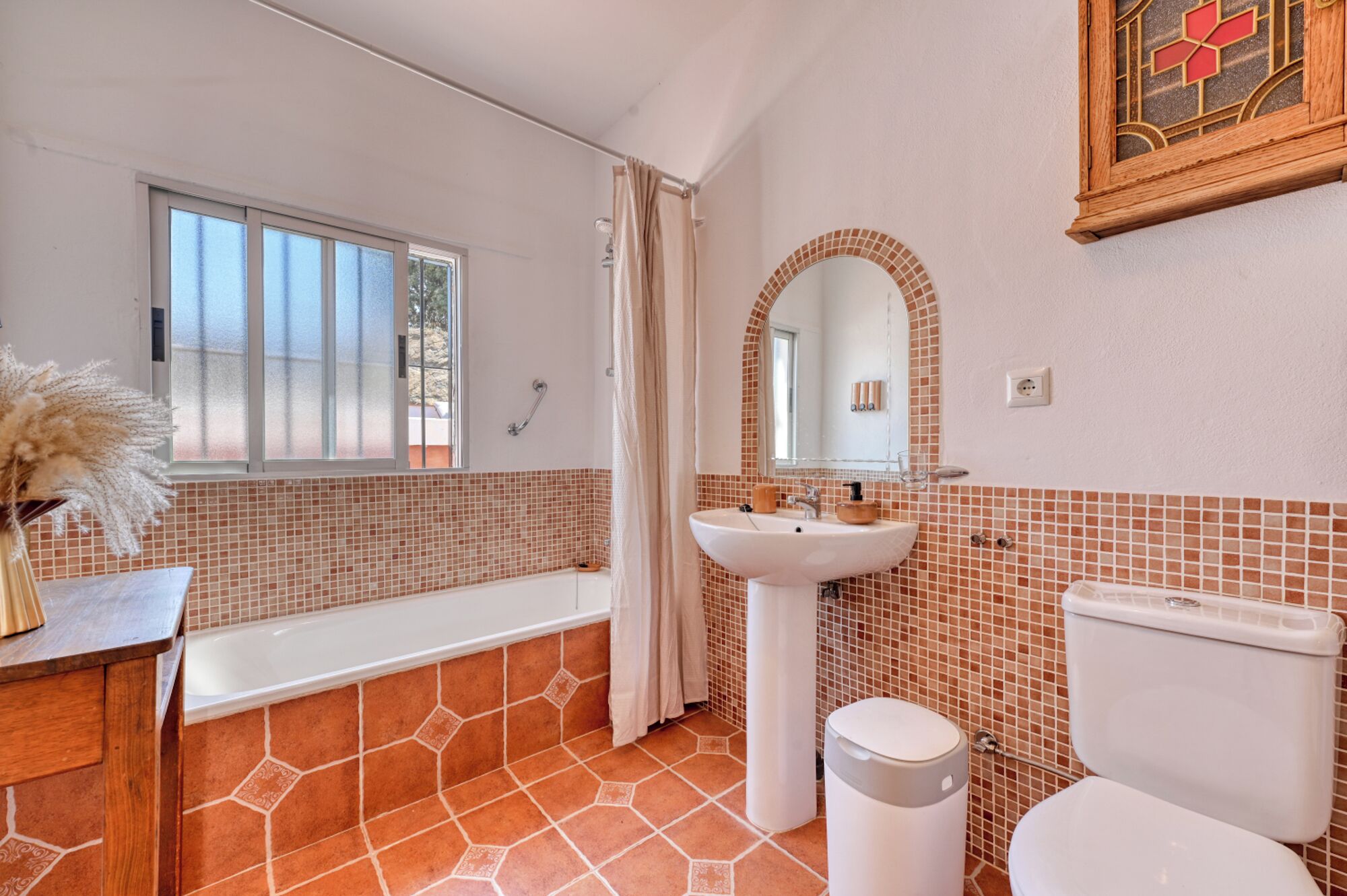 A bathroom with a bathtub, sink, and toilet, featuring tiled walls and a window.