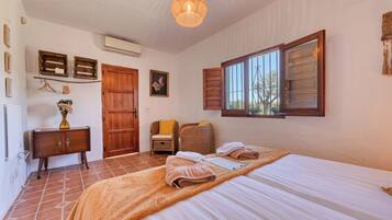A bedroom with a bed, a wooden wardrobe, a wicker chair, a hanging light fixture, and a window with shutters.