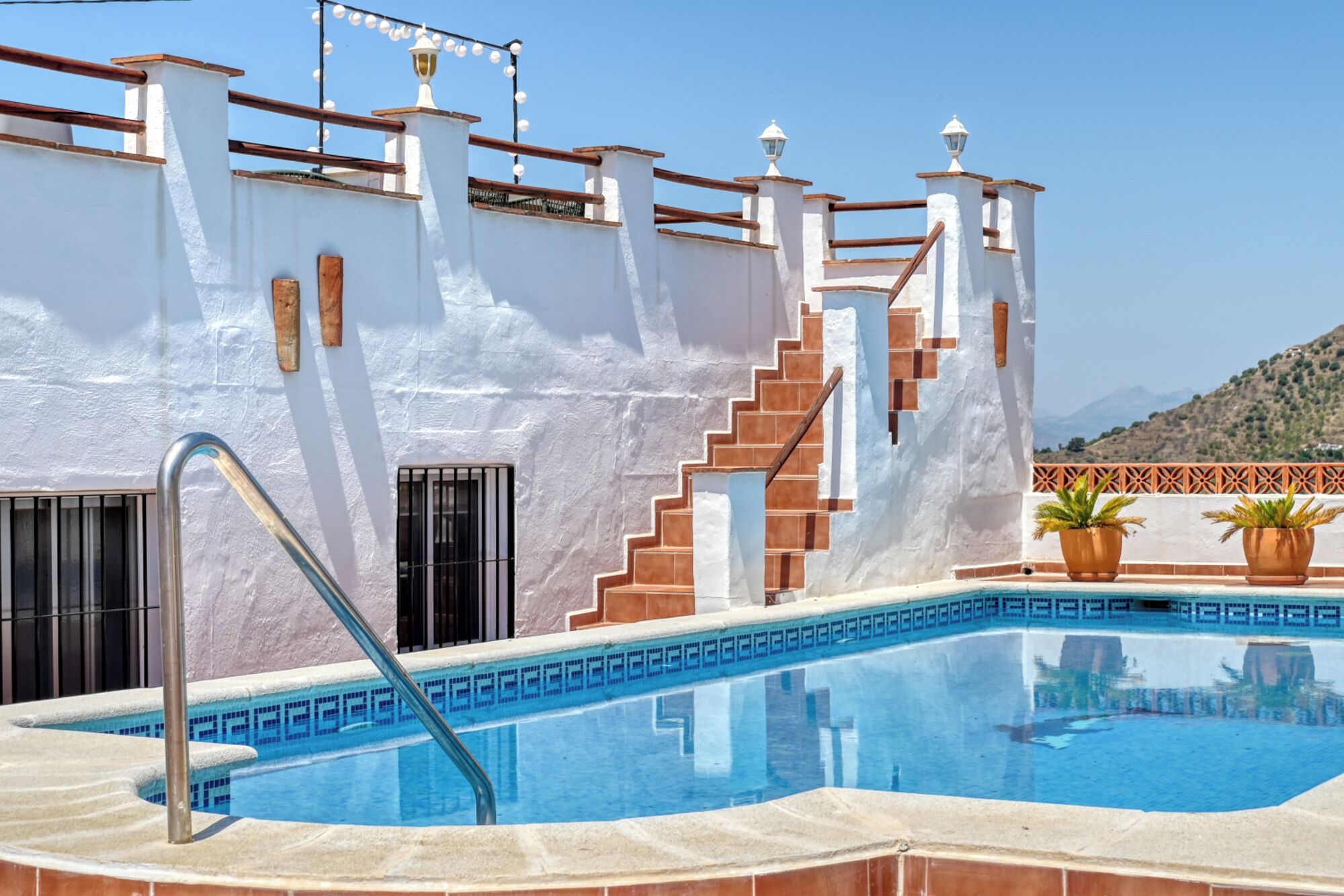 A swimming pool with a metal ladder, a staircase, and a white building with brown accents.