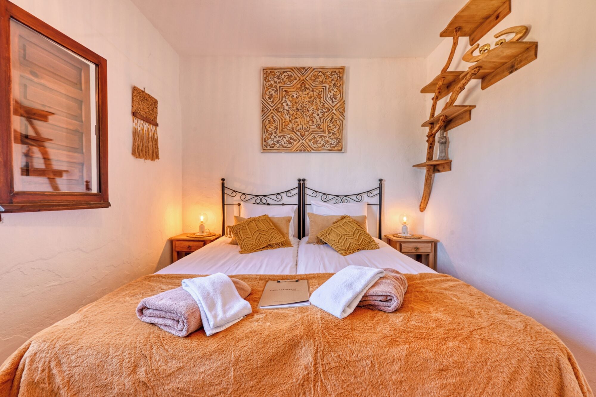 Un dormitorio con una cama, dos mesitas de noche, una obra de arte en la pared y un estante de madera.