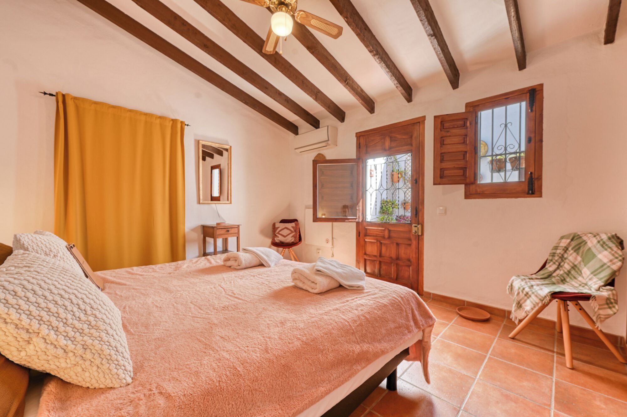 A bedroom with a bed, a chair, a wooden door, a window, and a ceiling fan.