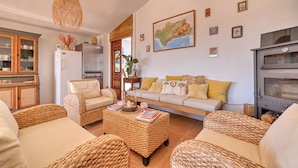 A living room with wicker furniture, a sofa with cushions, a refrigerator, a map on the wall, and a kitchen area with a stove. - Casa Azafranes Boutique B&B (Arenas)