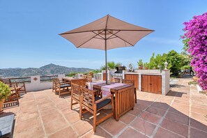 Eine Terrasse mit Tisch und Stühlen, einem Grill und Blick auf die Hügel.