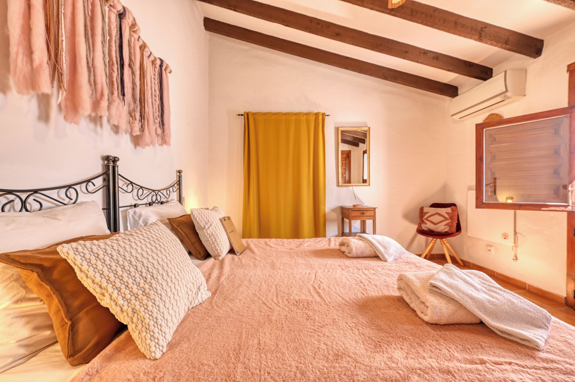 A bedroom with a bed, a wooden headboard, a mirror, a small table, and a window with curtains.