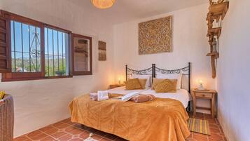 A bedroom with a bed, a window, a wall hanging, and a nightstand.
