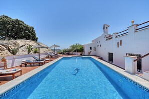 Ein Swimmingpool mit Liegestühlen und Sonnenschirmen, umgeben von einem weißen Gebäude mit einem Ziegeldach.