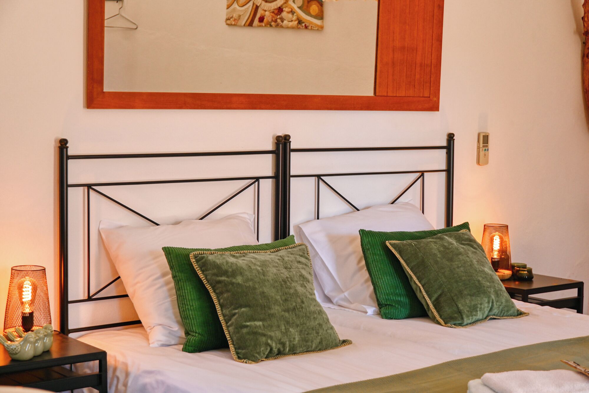 A bed with a metal frame, two pillows, a bedside table with a lamp, and a wall clock.
