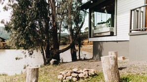 Una cabaña junto al lago con un hogar de piedra, postes de madera y una ventana con vistas al agua.