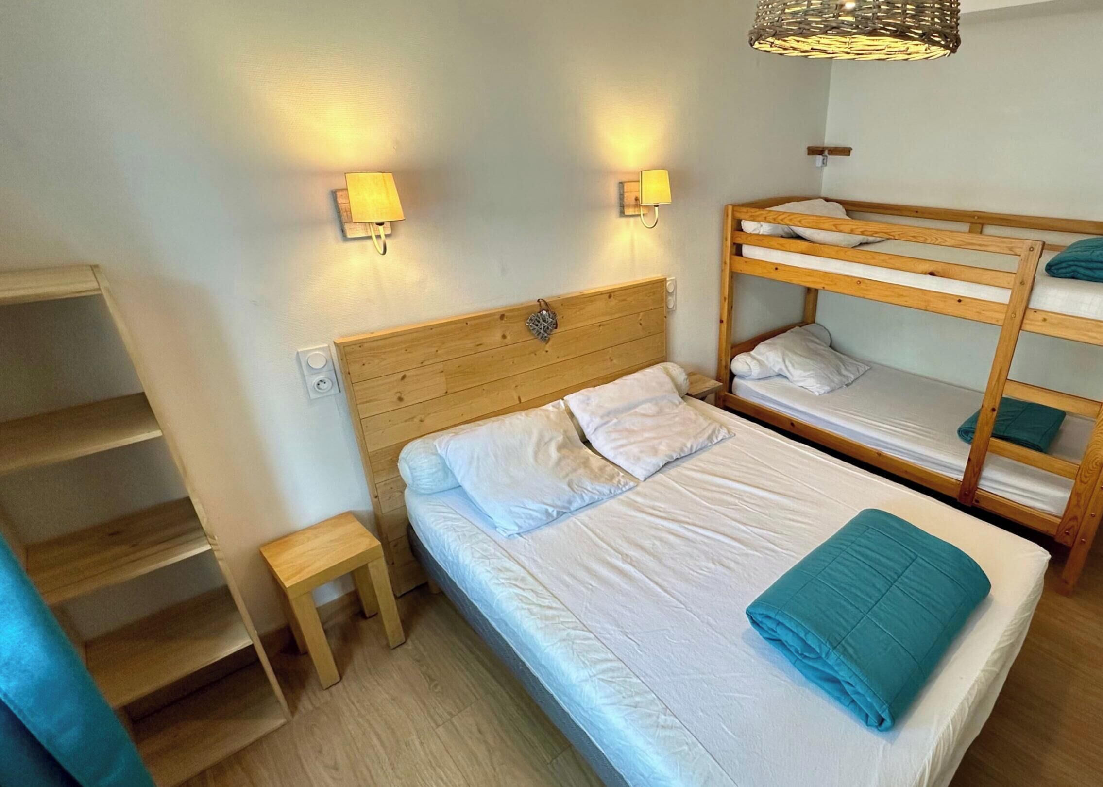 Ein Schlafraum mit Etagenbetten, einem Holz-Kopfteil, einem kleinen Holzschemel und zwei Wandleuchten.