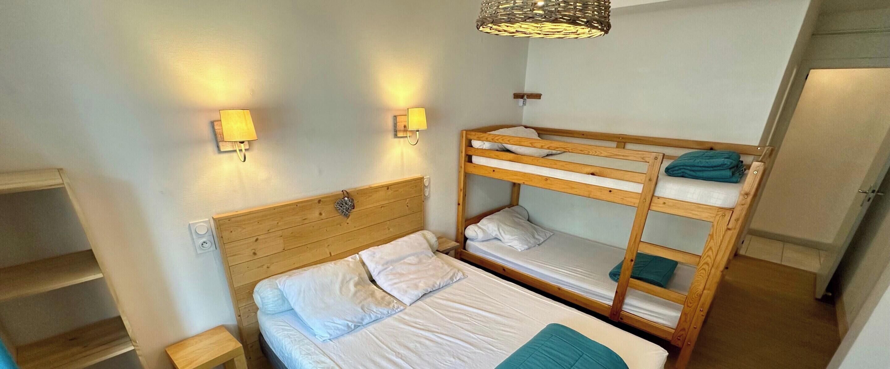 Ein Zimmer mit Etagenbett, einem Einzelbett, zwei Wandleuchten und einer Pendelleuchte.