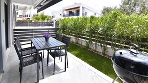An outdoor patio with a table and chairs, a grill, and a view of a residential area. - Renata Apartment in Nikiti (Sithonia)
