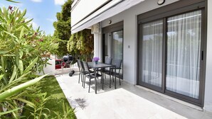 A modern outdoor patio with a dining table and chairs, a barbecue grill, and a sliding glass door leading to a covered area. - Renata Apartment in Nikiti (Sithonia)