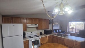 A kitchen with wooden cabinets, a white refrigerator, a stove, a microwave, and a dining table with chairs. - Norfork Lakeview Oasis House #12 at Teal Point Resort (Mountain Home)