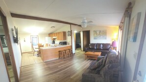 A spacious living area with a wooden floor, a sofa, a coffee table, and a kitchen in the background. - Norfork Lakeview Oasis House #12 at Teal Point Resort (Mountain Home)