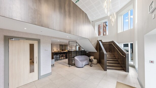 A spacious lobby with a modern staircase, a seating area, and a visible kitchen in the background. - Comfy 2 BR+ Free Parking Gym, Game Rooms, & Cinema (London)