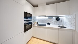 A modern kitchen with white cabinetry, a black oven, and a white countertop with a sink and a hexagonal backsplash. - Comfy 2 BR+ Free Parking Gym, Game Rooms, & Cinema (London)