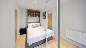 Une chambre moderne comprenant un lit, des tables de chevet, une bibliothèque intégrée et une cloison en verre.