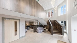 Un'ampia hall con una moderna scala, un'area salotto e una cucina visibile sullo sfondo.