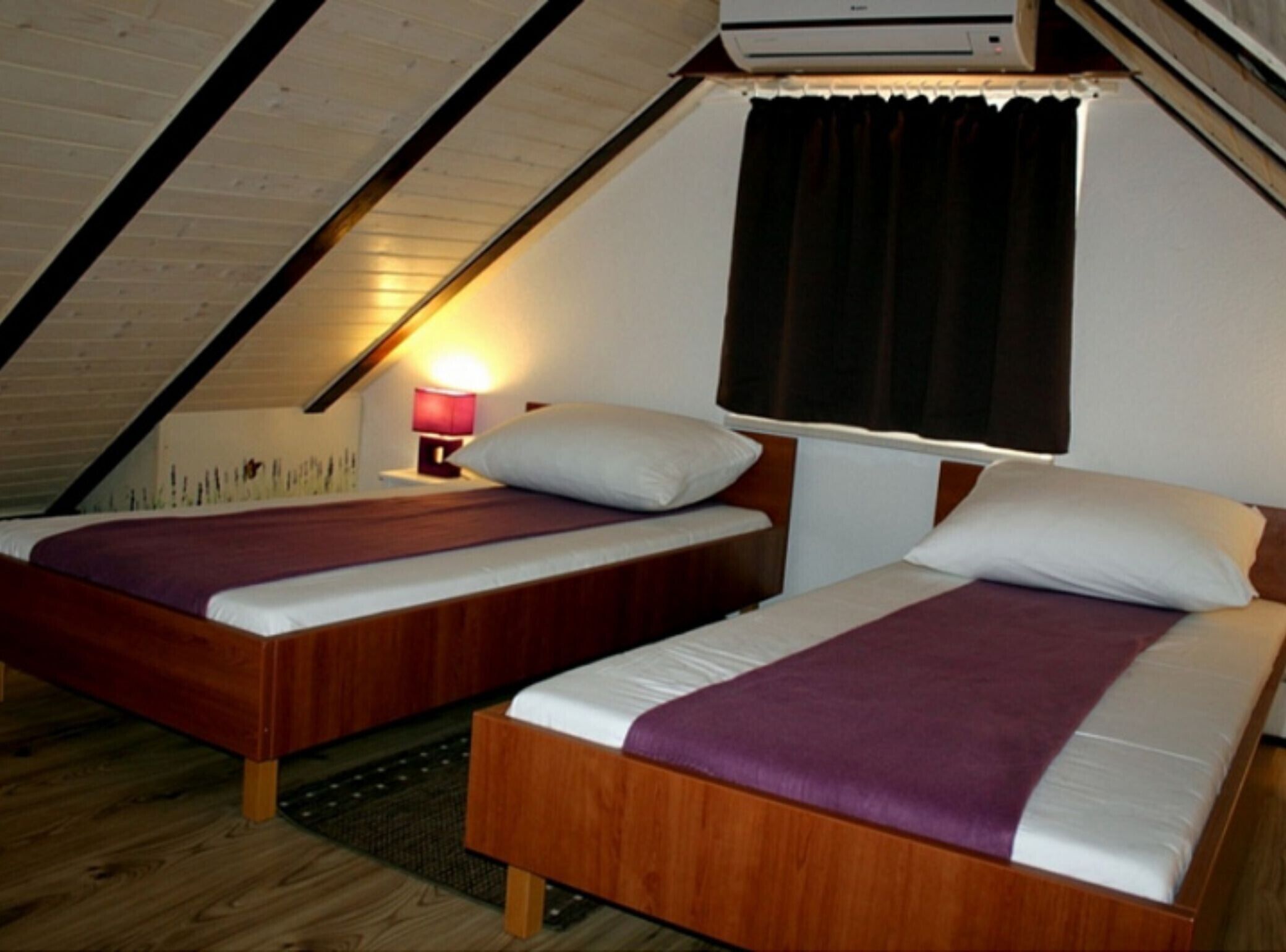 Een kleine, knusse kamer met twee houten bedden, een nachtkastje met een lamp en een raam met gordijnen.