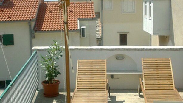 A rooftop terrace with two wooden lounge chairs, a potted plant, and a small table.