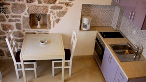 A small kitchen with a stone wall, a table with chairs, a coffee maker, and a sink.